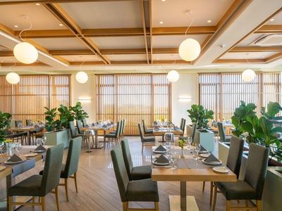 Helles Restaurant mit Holzbalkendecke, grünen Pflanzen, Holztischen und gepolsterten Stühlen.
