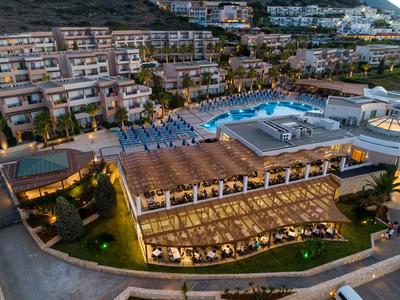 Hotelanlage mit beleuchtetem Pool, Sofas und Stühlen, umgeben von Terrassen und Gebäuden.