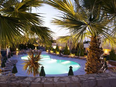 Ein beleuchteter Pool umgeben von Palmen und Sitzgelegenheiten in der Abenddämmerung.