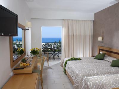 Helles Hotelzimmer mit Doppelbett, TV, Balkon und Blick auf das blaue Meer.