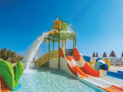 Wasserrutsche im Pool mit bunten Rutschen und Wasserstrahl unter klarem blauem Himmel.