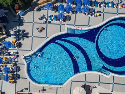 Großer, blau geschwungener Hotelpool mit Liegestühlen und Gästen an einem sonnigen Tag.