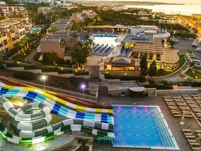 Bunt beleuchteter Wasserpark mit Rutschen und großem Pool in urbaner Abendlandschaft.