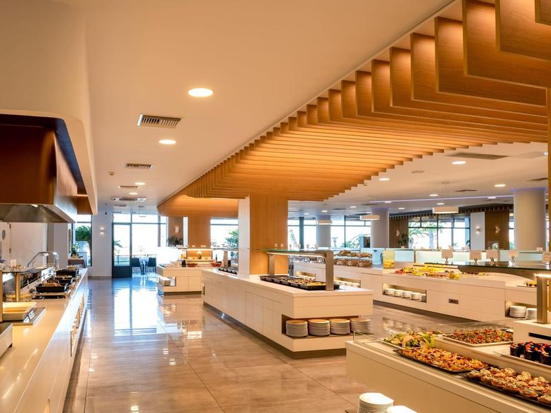 Área moderna de buffet en hotel con techos de madera y estaciones de comida bien iluminadas.