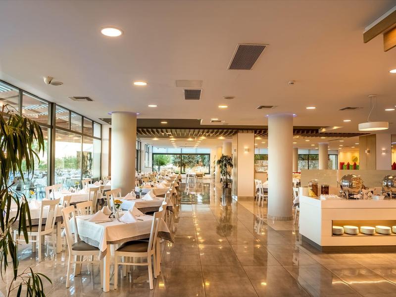 Restaurante de hotel moderno y luminoso con mesas blancas y grandes ventanales durante el día.