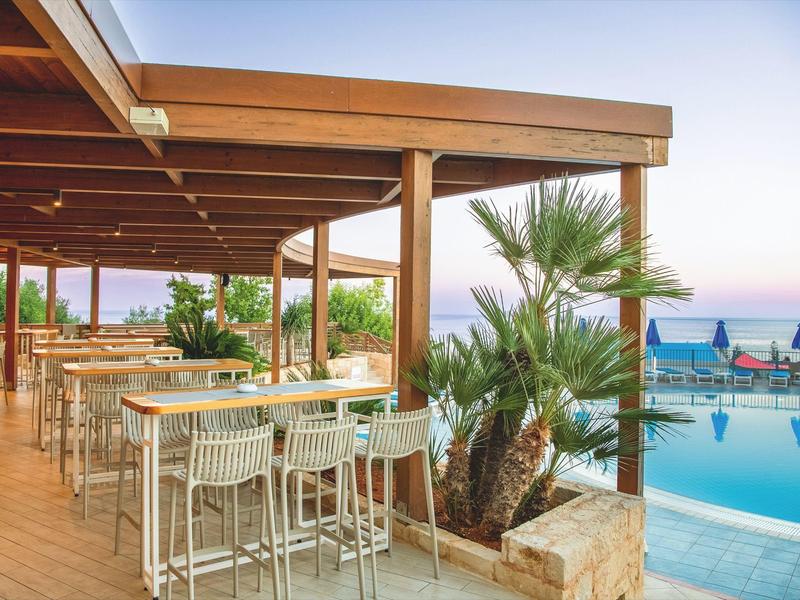Terraza de restaurante junto a piscina con sillas altas y vista al mar al atardecer.