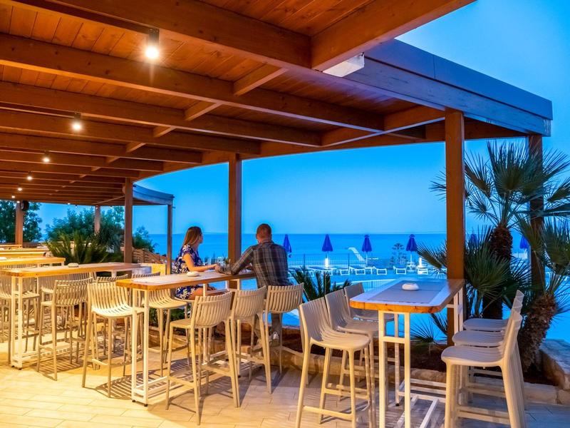 Terraza exterior cubierta de un restaurante con vista al mar en la noche, iluminada con luz cálida.