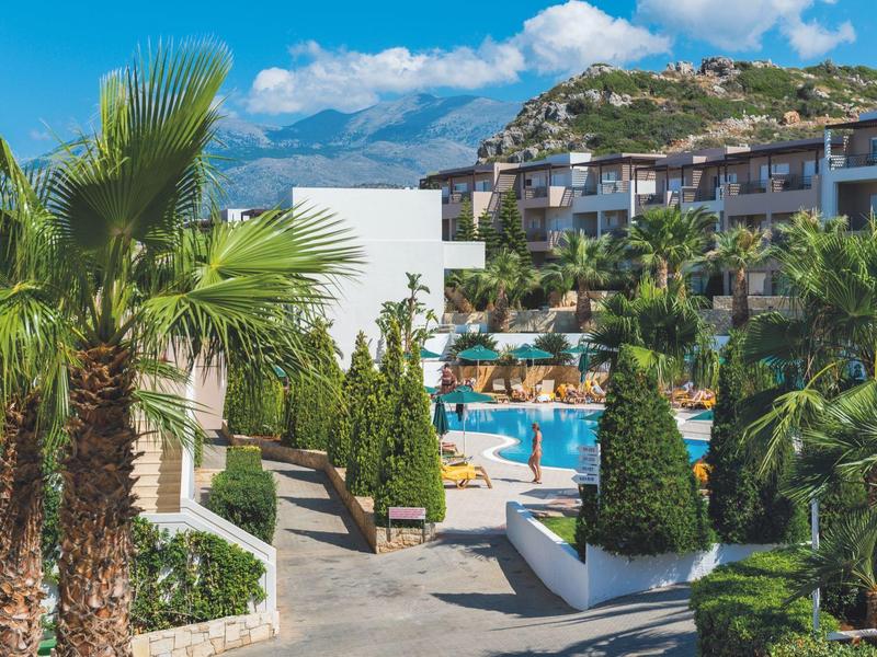 Complejo hotelero con piscina, palmeras y vistas a colinas boscosas bajo cielo azul.