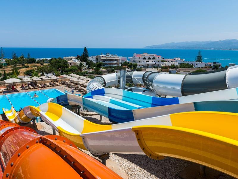 Toboganes de agua coloridos conducen a una piscina en un resort costero soleado con vista al mar.
