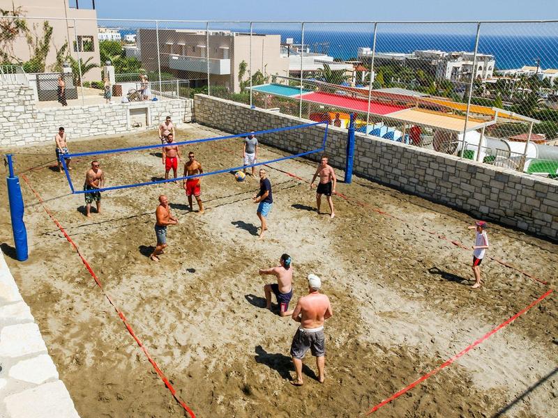 Personas jugando voleibol en una cancha al aire libre con vistas al mar y edificios cercanos.
