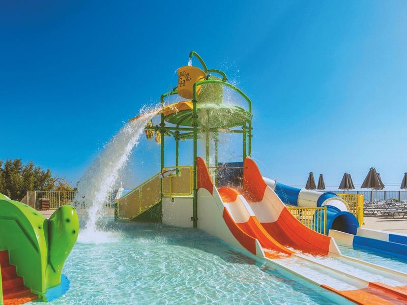 Parque acuático con toboganes de colores y torre de juego bajo un cielo azul despejado.