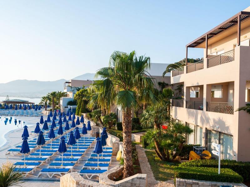 Terraza de hotel con sombrillas azules, palmeras y vista a la montaña en la mañana.