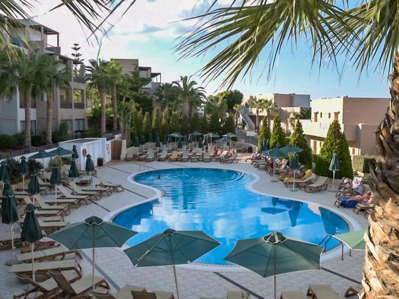 Piscina del hotel con tumbonas y sombrillas, rodeada de palmeras y edificios del hotel.