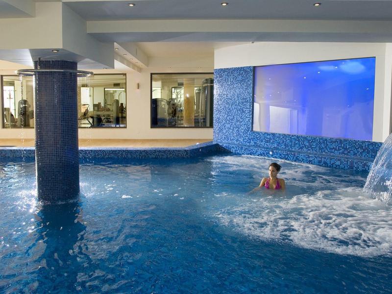 Piscina interior con juegos de agua y área de descanso en un hotel moderno.