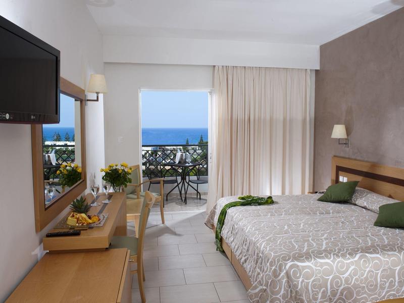 Habitación de hotel luminosa con cama, balcón y vista al mar, decoración moderna y sencilla.