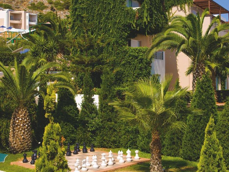 Jardín del hotel con palmeras tropicales, vegetación densa y gran juego de ajedrez al aire libre.