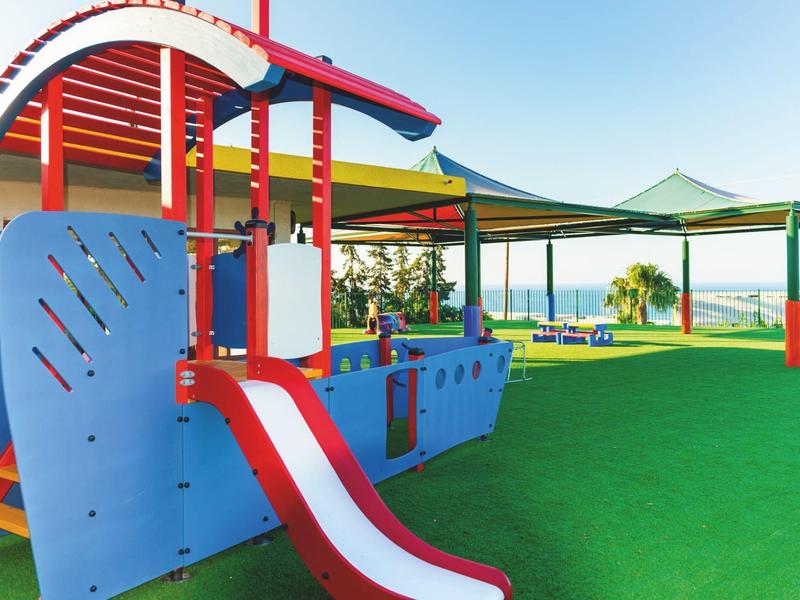 Zona de juegos colorida con tobogán y sombra en un área verde al aire libre.