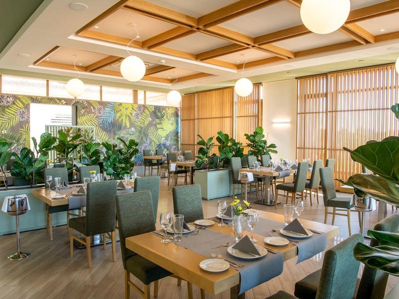 Restaurante moderno y luminoso con elementos de madera, plantas verdes y mesas preparadas.
