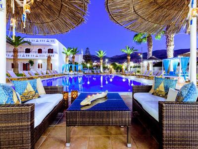 Bequeme Sitzgelegenheiten mit Kissen neben einem beleuchteten Pool in einem tropischen Hotelresort bei Nacht.