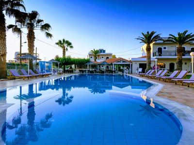 Bazén s lehátky a palmami před budovou hotelu za jasné oblohy.