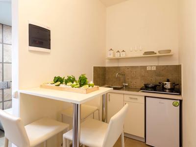 Malý kuchyňský kout se stolem, dvěma bílými židlemi a kuchyňským náčiním v světlé místnosti.