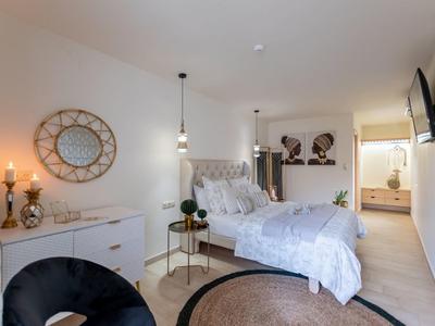 Světlá ložnice s kulatým kobercem, bílým nábytkem a dekorativním nástěnným zrcadlem