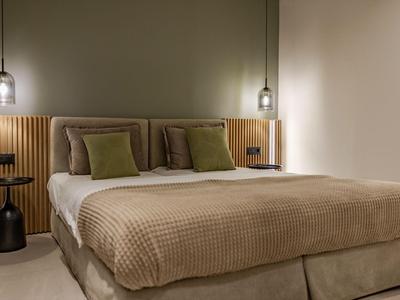 Habitación de hotel moderna con cama grande, colcha beige y dos almohadas verdes.