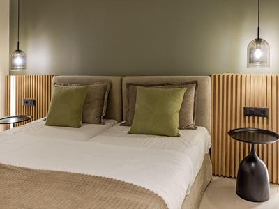 Habitatión de hotel moderna con cama doble, cojines verdes y paneles de madera cálidos.