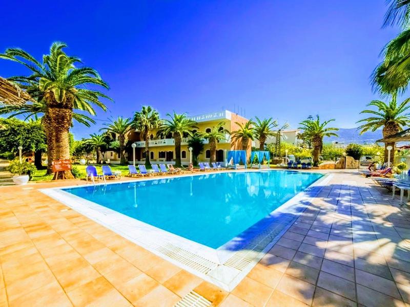 Jasně modrý bazén obklopený palmami a lehátky pod jasně modrou oblohou.