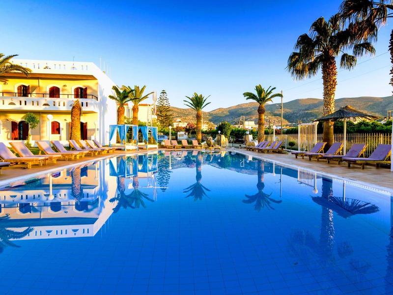 Velký hotelový bazén s lehátky a palmami pod jasně modrou oblohou.