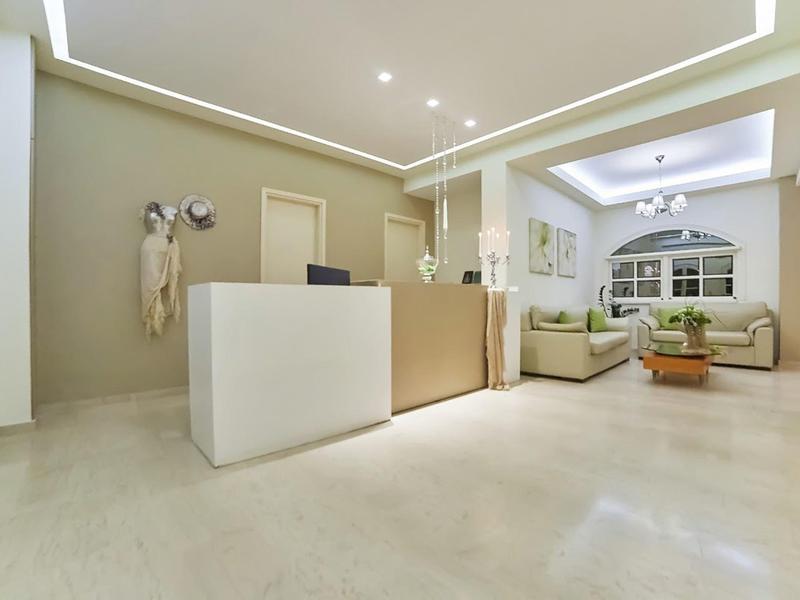 Světlá hotelová recepce s pultem, pohovkami a moderním osvětlením.