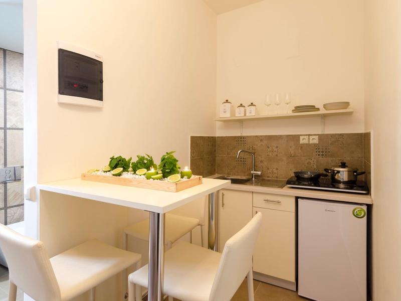 Malý kuchyňský kout se stolem, dvěma bílými židlemi a kuchyňským náčiním v světlé místnosti.