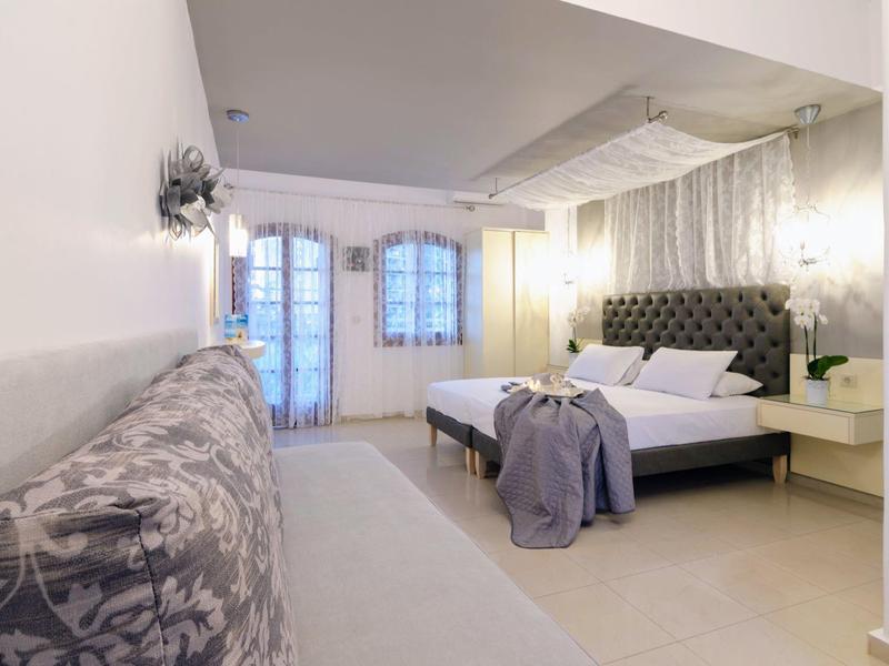 Moderní ložnice s čalouněnou postelí, lavičkou, velkými okny a světlými stěnami.