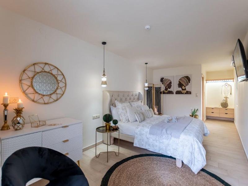 Světlá ložnice s kulatým kobercem, bílým nábytkem a dekorativním nástěnným zrcadlem