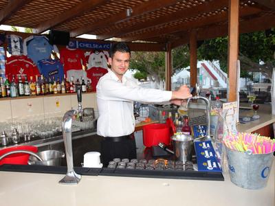 Mann in weißem Hemd zapft Bier an Holztresen mit Bierzapfanlagen und bunten Trinkhalmen.