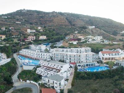 Panorama einer Hügelanlage mit weißen Mehrfamilienhäusern, Straßen und einem blauen Schwimmbecken.