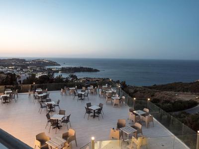 Große Dachterrasse mit vielen Tischen und Stühlen, im Hintergrund Meer und Küstenlinie bei Dämmerung.
