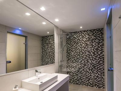 Moderner Badbereich mit großem Spiegel, weißem Waschbecken und Wand mit schwarzen Fliesenmosaiken.