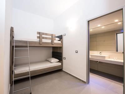 Kleiner Raum mit grauem Etagenbett und angrenzendem Badezimmer mit Doppelwaschbecken.