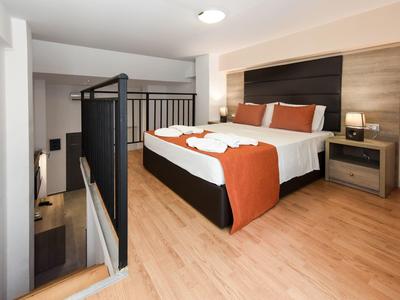 Modernes Schlafzimmer mit Holzboden, Doppelbett, orangefarbenen Kissen und Metallgeländer am Treppenabgang.