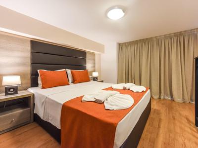 Sauberes Schlafzimmer mit Doppelbett, orange-weißer Bettwäsche, Nachttischen und Vorhängen.