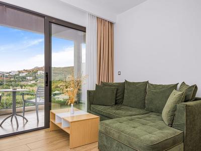 Helles Wohnzimmer mit grünem Ecksofa, kleinem Holztisch und Blick auf Balkon mit Stuhl und Tisch.
