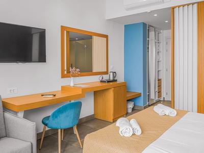 Modernes Hotelzimmer mit Bett, Holzschreibtisch, blauem Stuhl und großem Spiegel an weißer Wand.