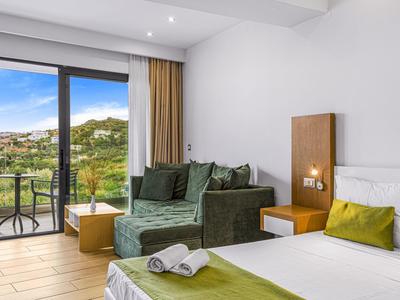 Helles Schlafzimmer mit grünem Sofa, weißem Bett, Holzmöbeln und Balkon mit Bergblick.