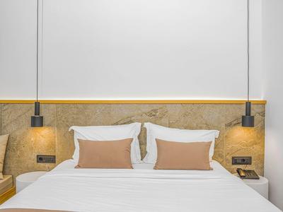 Modernes Schlafzimmer mit großem Bett, weißen Kissen, braunen Zierkissen und zwei Hängelampen.