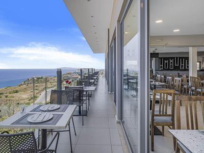 Stoly na balkóně s výhledem na moře a interiér restaurace za jasného počasí.