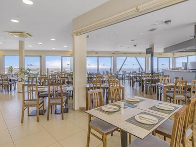 Helle, geräumige Cafeteria mit vielen Holztischen und Stühlen, Fenster mit Meerblick.