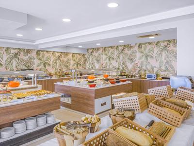 Moderní snídaňový bufet v světlé místnosti s dřevěnými pulty a posezením s ratanovými židlemi.