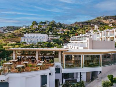 Moderní hotelový komplex na kopci s terasami a výhledem na okolí pod modrou oblohou.