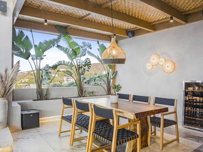 Otevřená jídelní část s dřevěným stolem, židlemi, rostlinami a moderním osvětlením na terase.